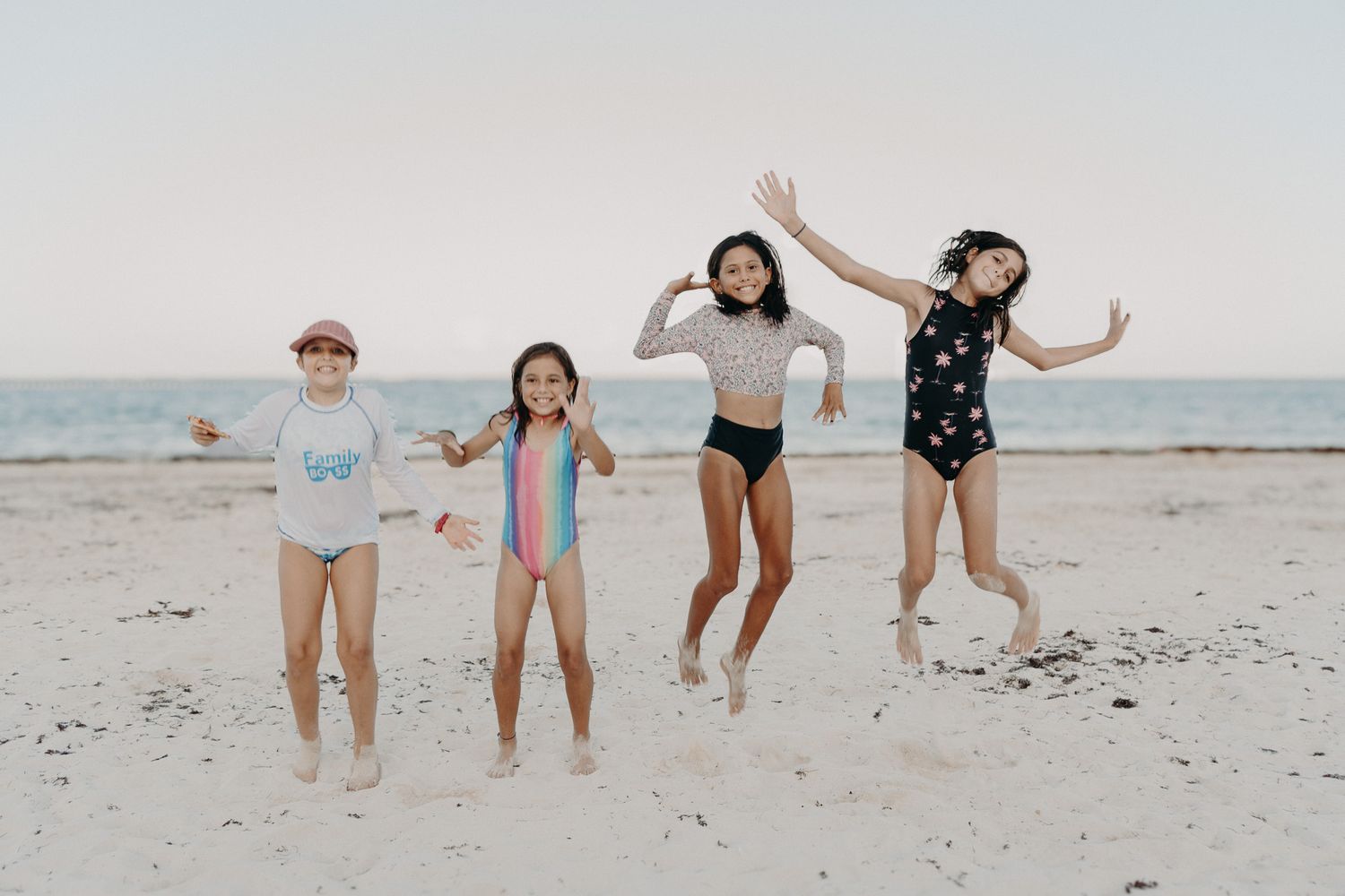 A joyful group in casual summer outfits and swimwear playing and jumping together on a sandy beach. Puerto Morelos Family Photography.