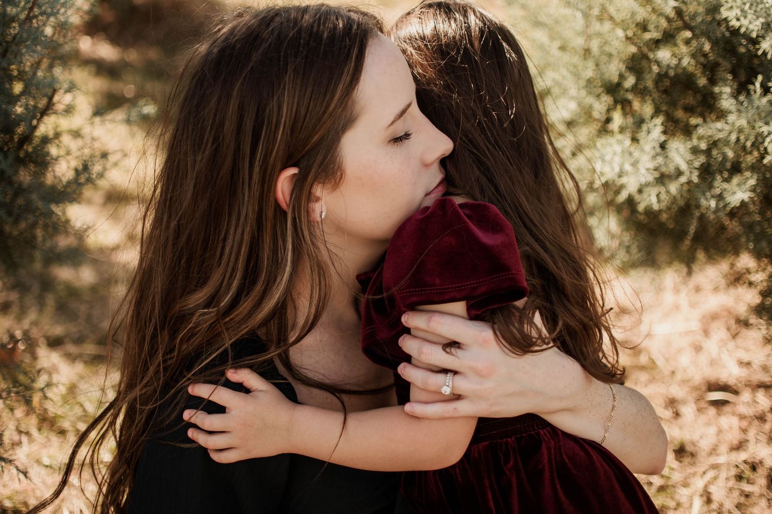 A tender embrace between two people in warm sunlit nature setting wearing burgundy clothing.
