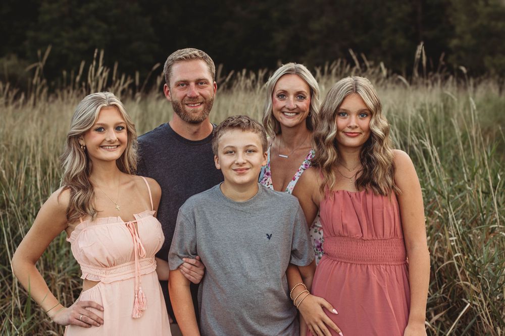 Family portrait session in muted tones against tall grass during golden hour.