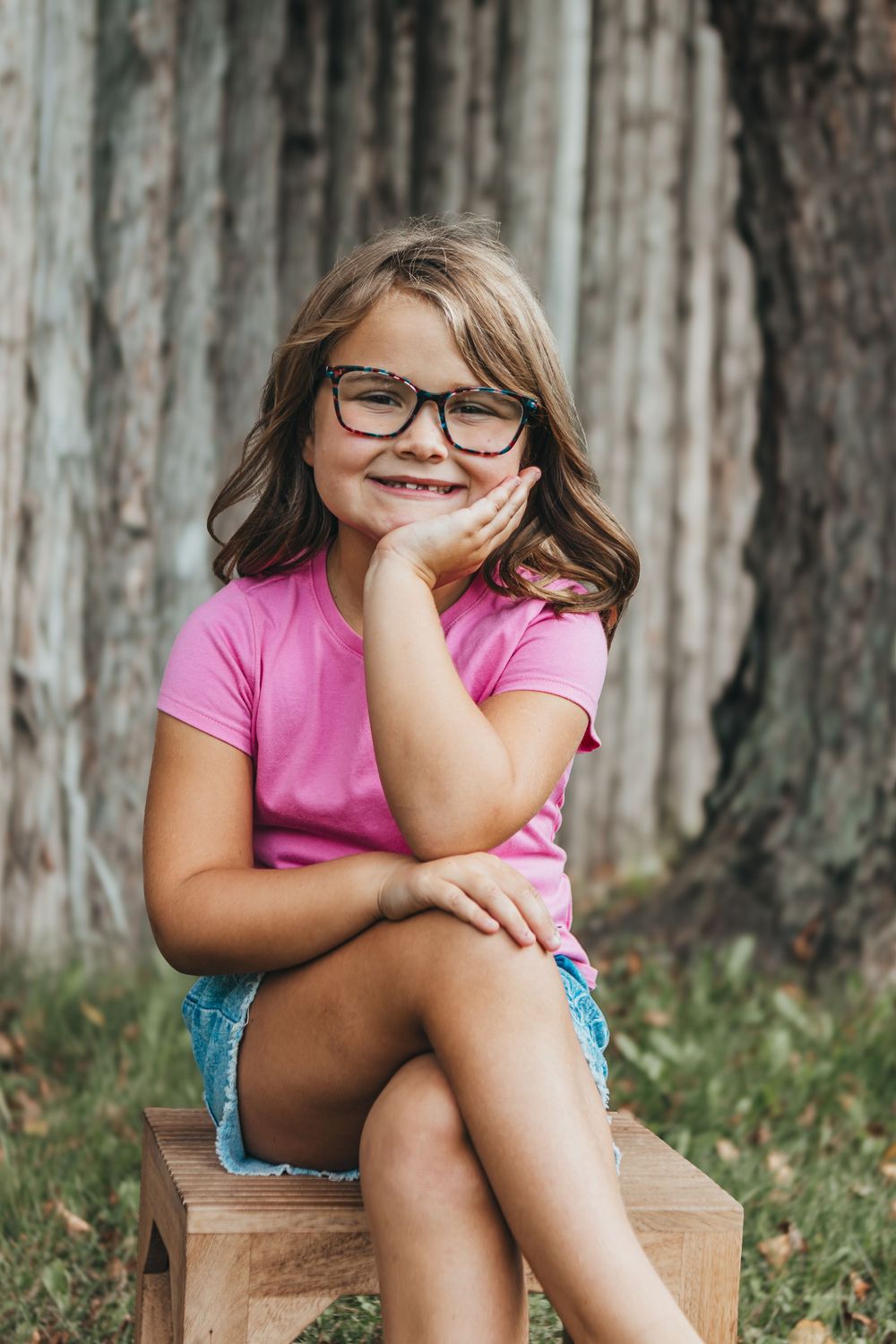 Candid portrait series of someone sitting on wooden stool wearing pink shirt and glasses.