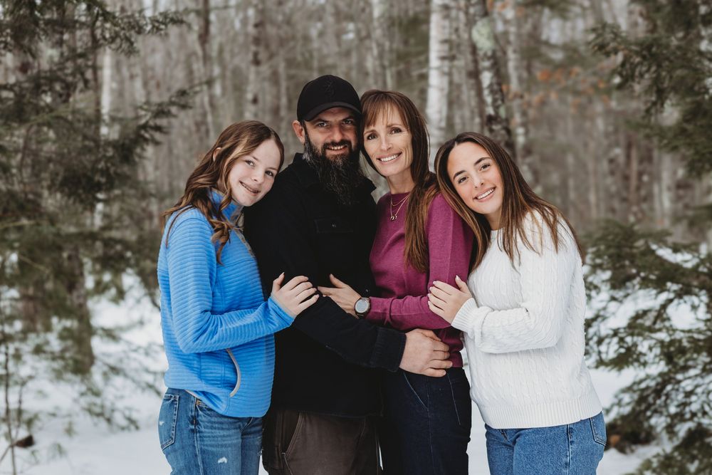 Family group photo session in a snowy forest setting with everyone wearing coordinated winter outfits.