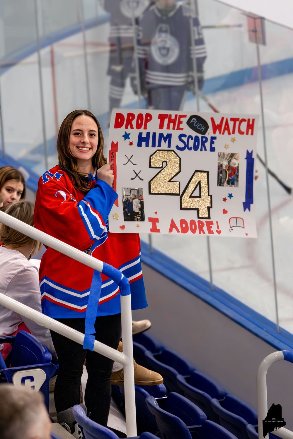 Hockey girlfriend cheers at a game with a homemade sign for her boyfriend.