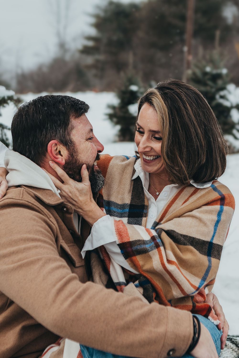 A romantic winter photoshoot with a couple wrapped in a plaid blanket sharing intimate moments.