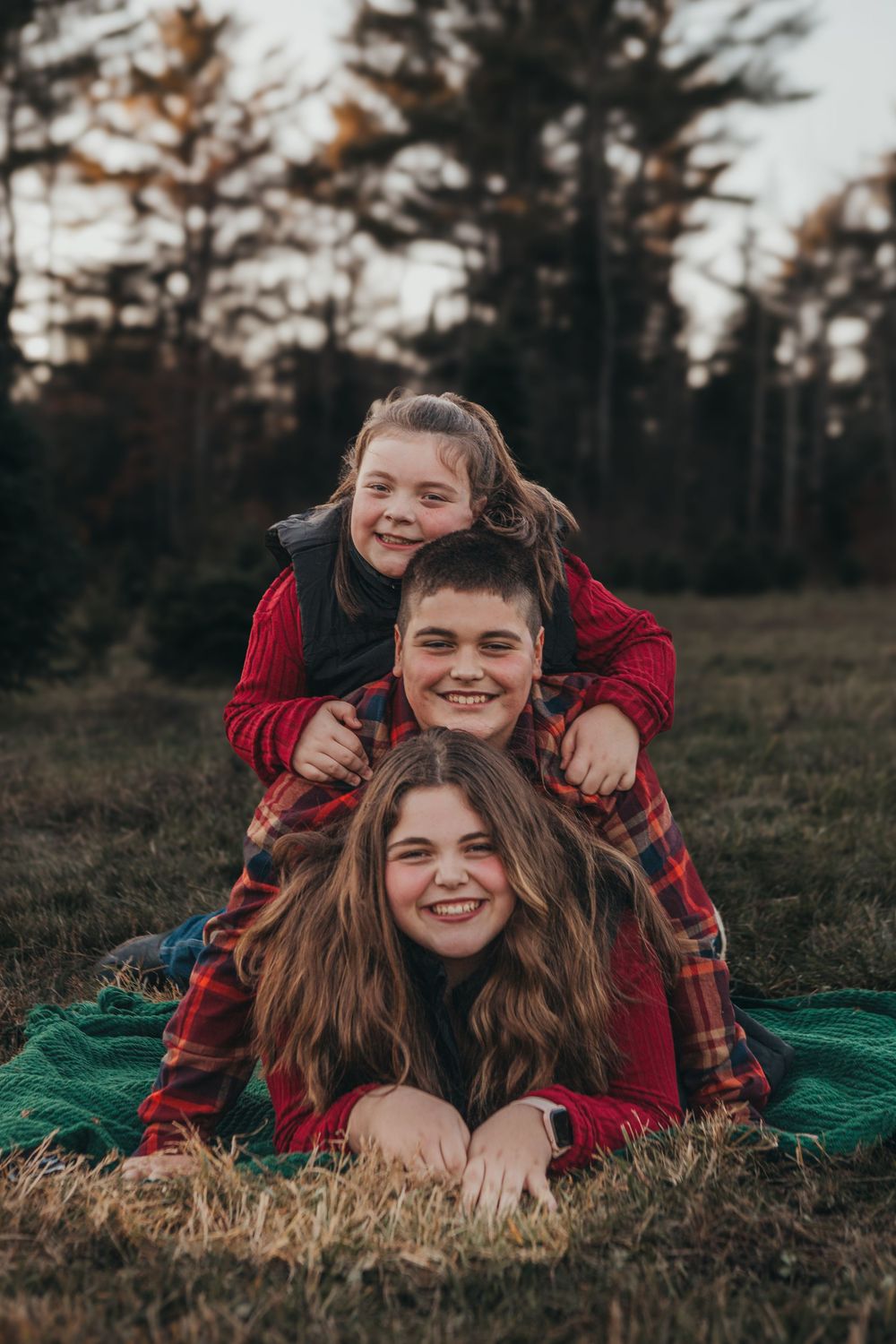 A playful outdoor family portrait with everyone laying on a green blanket in casual red clothing.