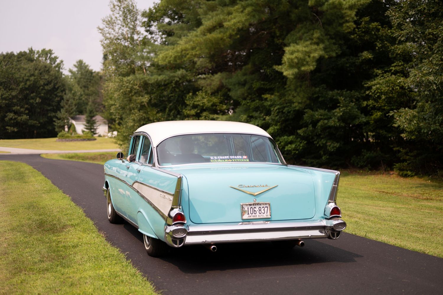 Classic turquoise Chevrolet car parked on a tree-lined road.