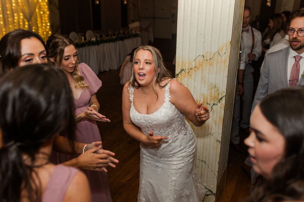 Wedding guests dance and celebrate on a crowded dance floor at an indoor reception venue.