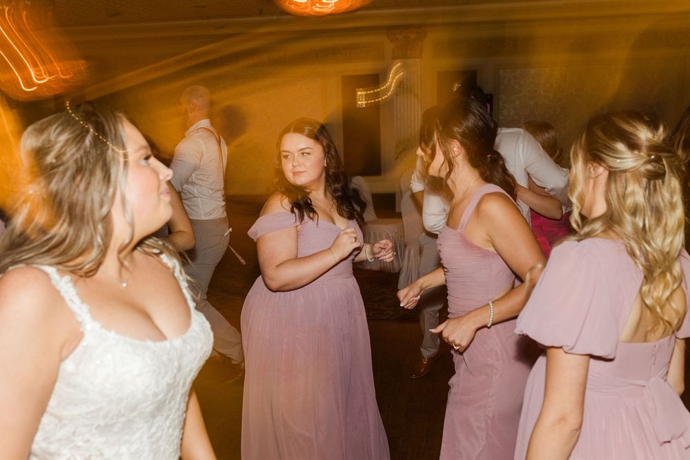 Wedding party members dance and celebrate together on a dimly lit dance floor at a reception.