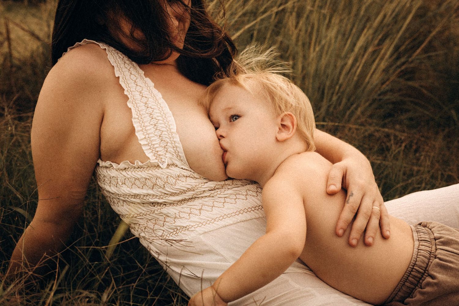 An intimate motherhood photography series shows tender moments of nursing in a golden-lit outdoor setting. Javea Photographer