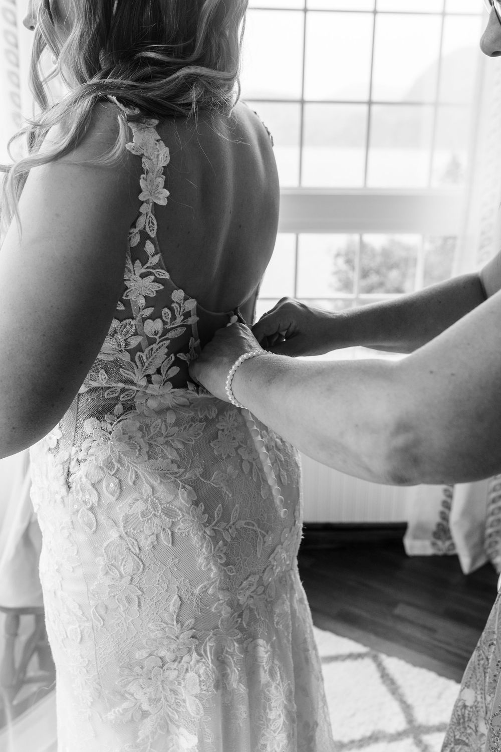 A bride wearing an ivory lace wedding gown gets ready in a sunlit room.