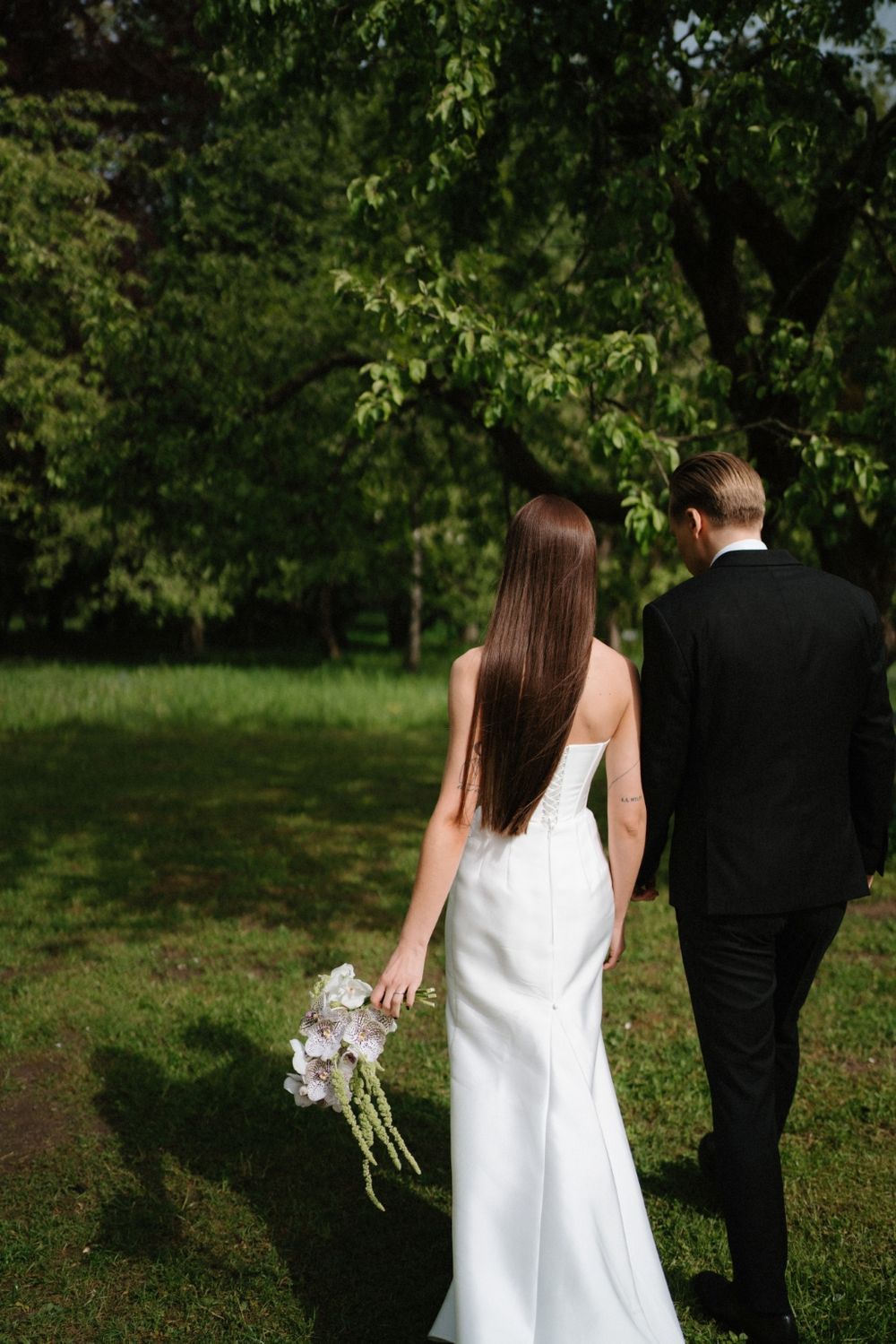 Bride and groom walking away through a lush green garden setting.