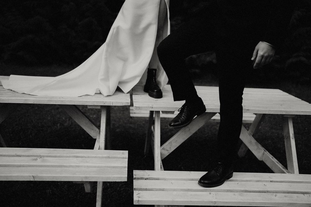 Black and white detail shot of wedding dress and suit on a wooden picnic table.
