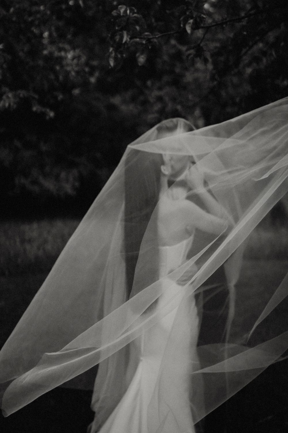 Artistic black and white photo showcasing flowing bridal veil in a garden setting.