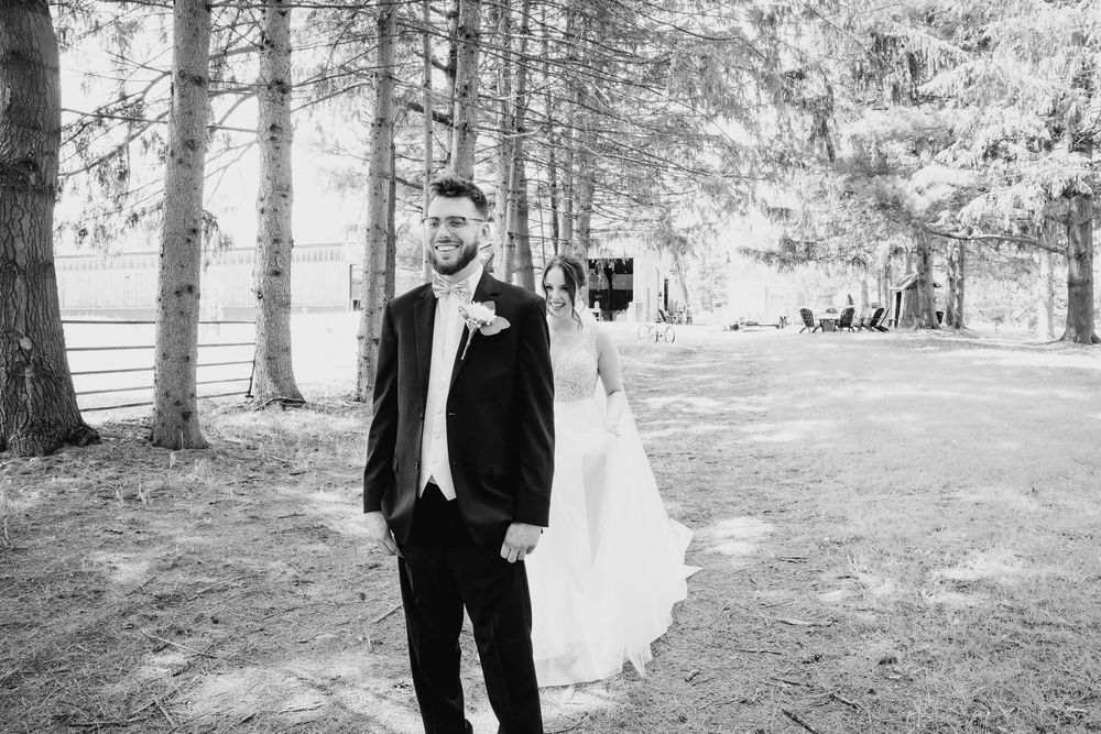 A wedding couple share a romantic moment while walking together among tall evergreen trees in a forest setting.