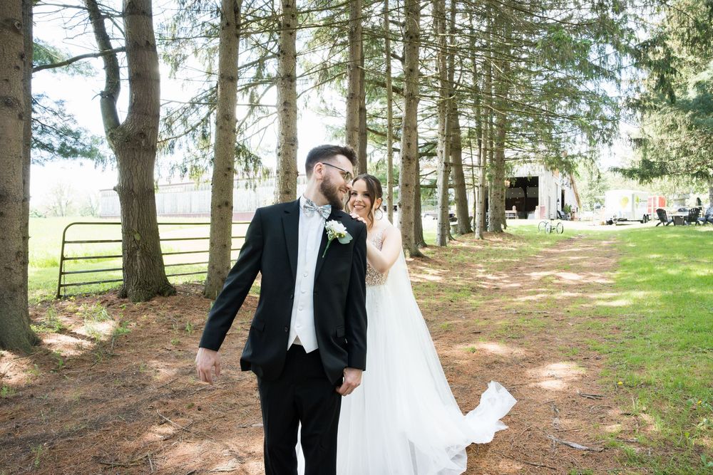 A romantic outdoor photo shoot captures a newlywed couple surrounded by tall pine trees in a wooded setting.