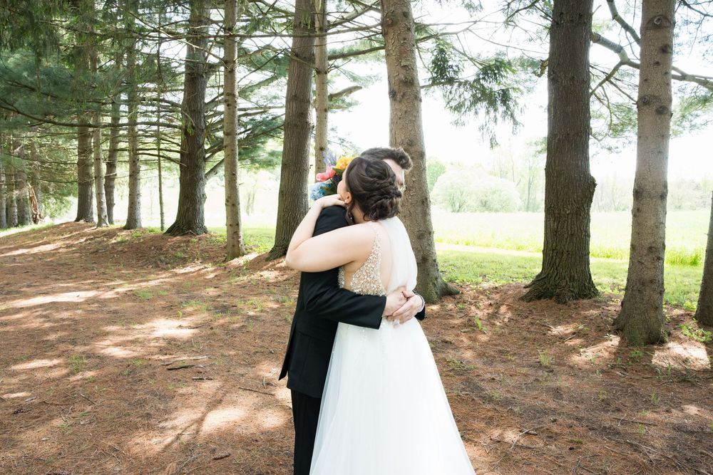 A couple in formal wedding attire embraces tenderly in a serene forest setting during their romantic photoshoot.
