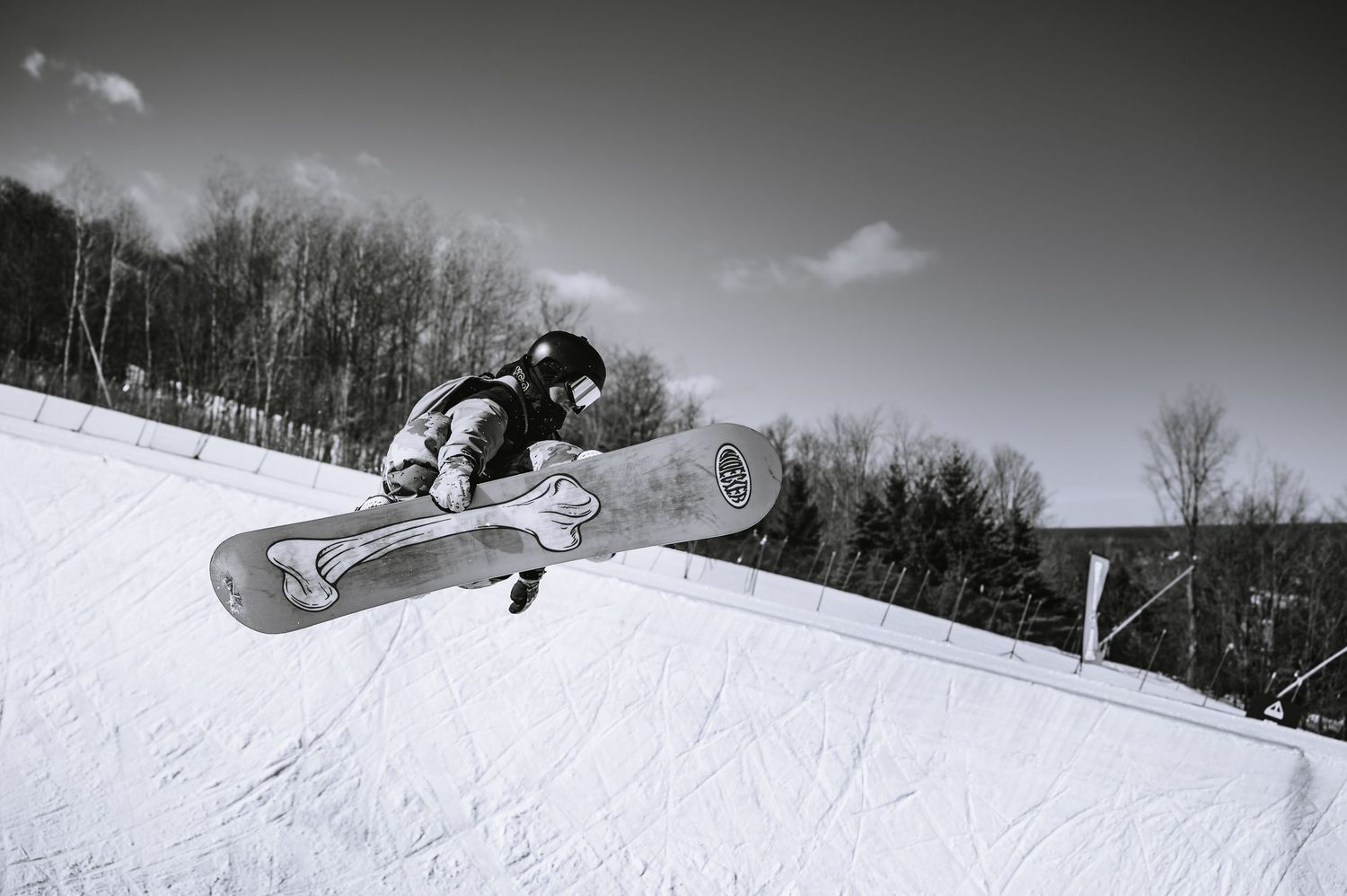 A snowboarder performs a mid-air jump on a snowy slope, captured in black and white against a winter landscape.