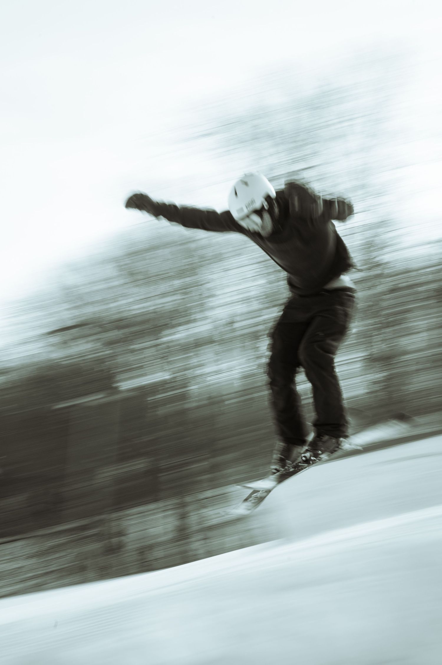 A blurred action shot of a skier jumping with arms outstretched against a snowy winter landscape.