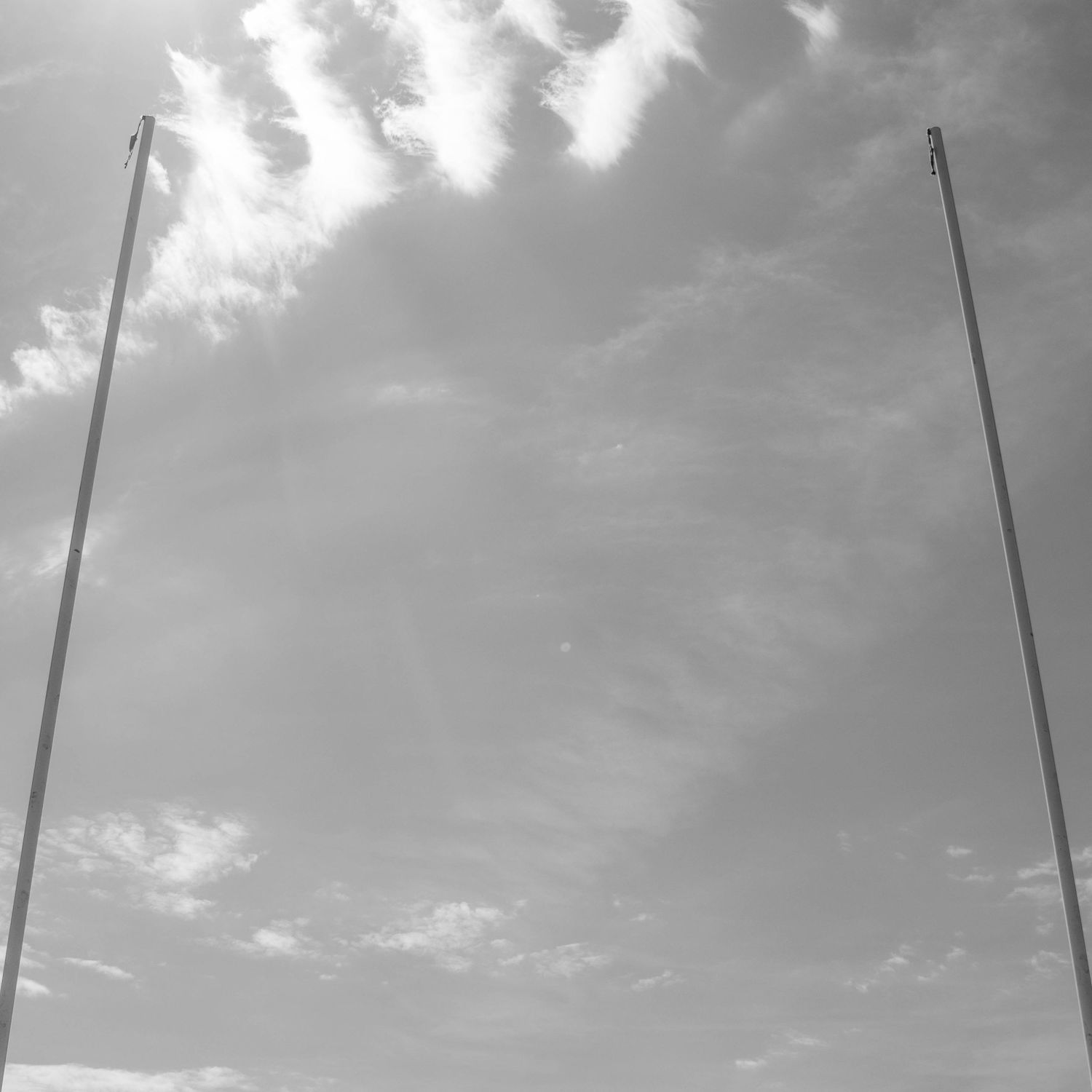 Black and white photo of two tall flagpoles against a cloudy sky.