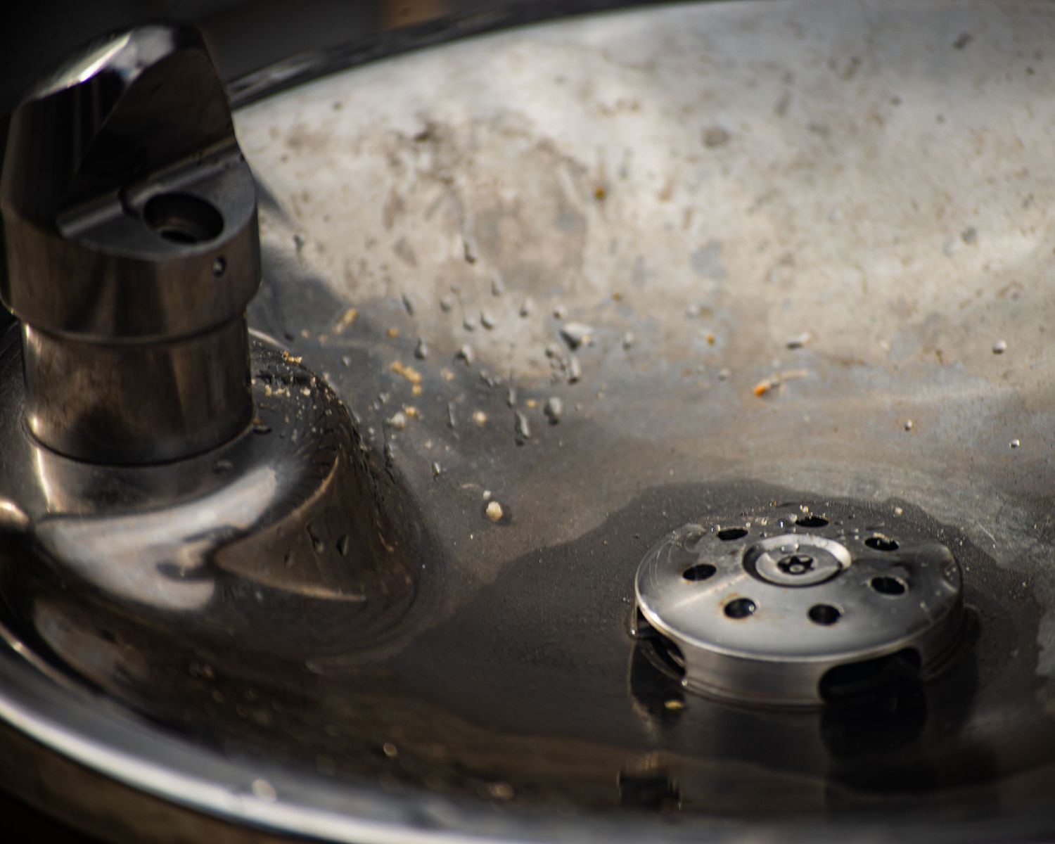 Macro close-up of metal mechanical parts submerged in oil inside a metallic bowl.