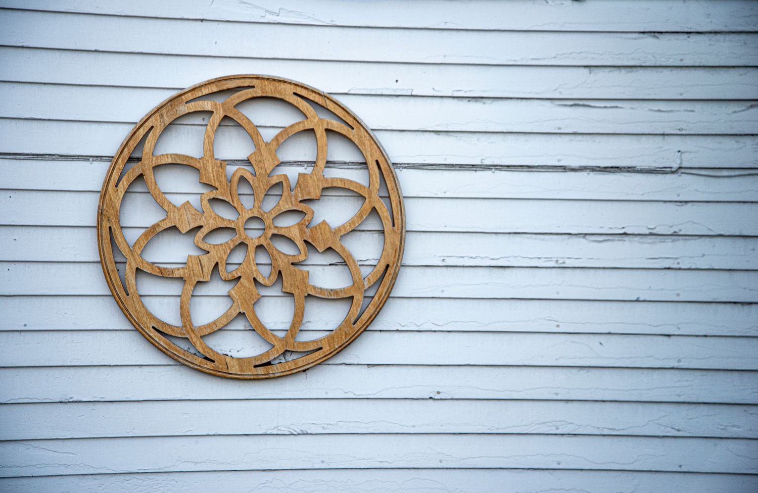 Decorative wooden mandala wall art mounted on white horizontal siding.
