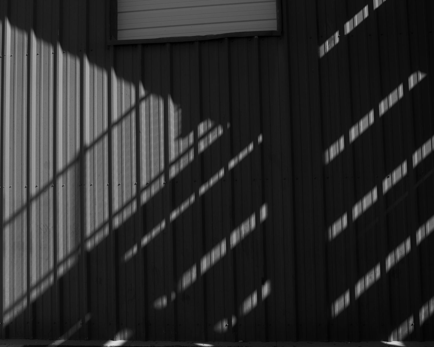 Black and white photo of diagonal shadow patterns on a corrugated metal wall.