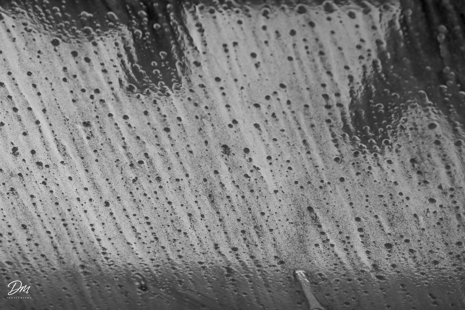 Black and white close-up of raindrops on a glass window creating abstract patterns.