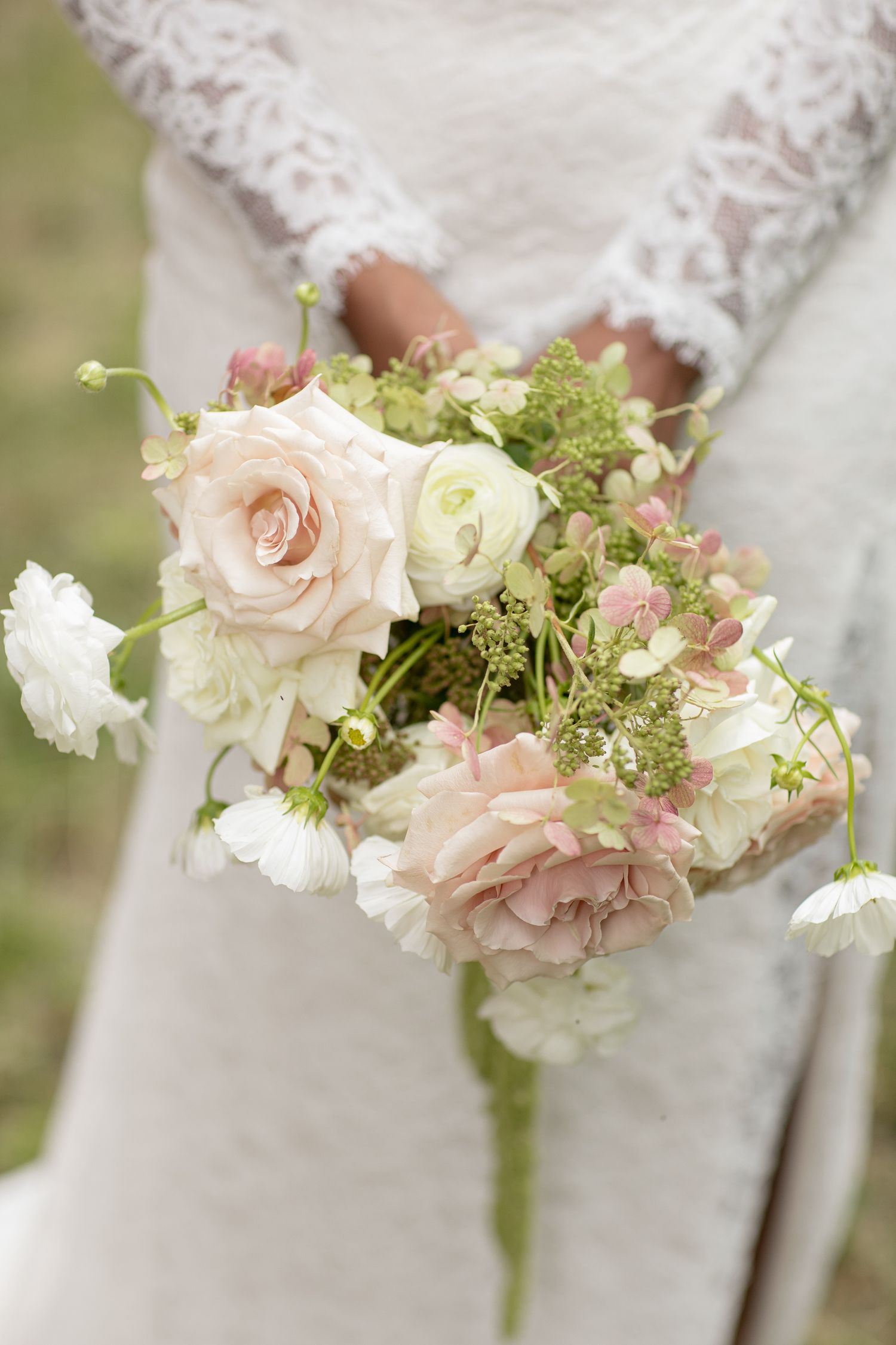 Close-up view of a delicate bridal bouquet featuring blush pink roses and white flowers with soft green accents.