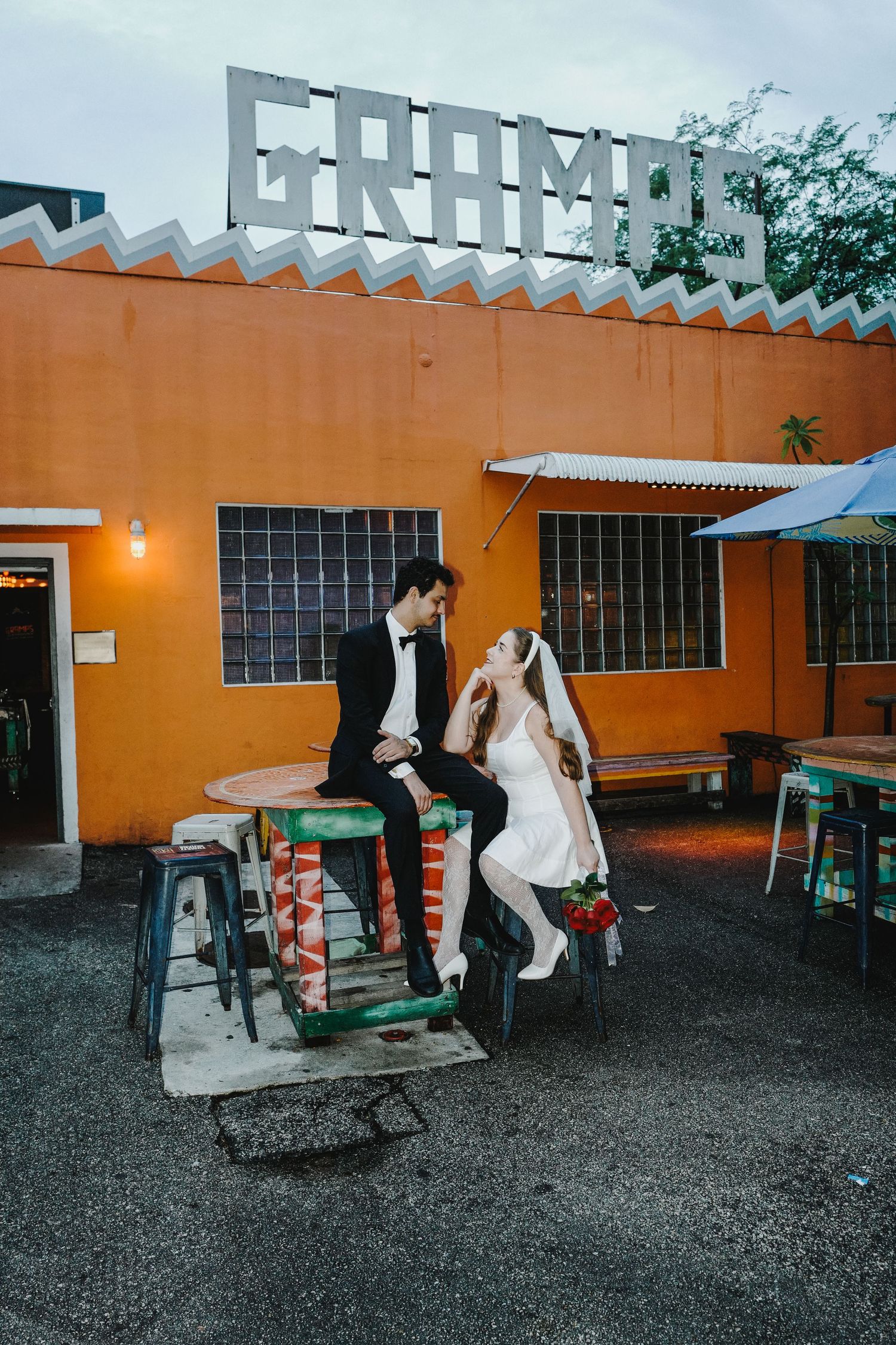 A sequence of people dancing and moving outdoors in front of an orange building wall with windows.