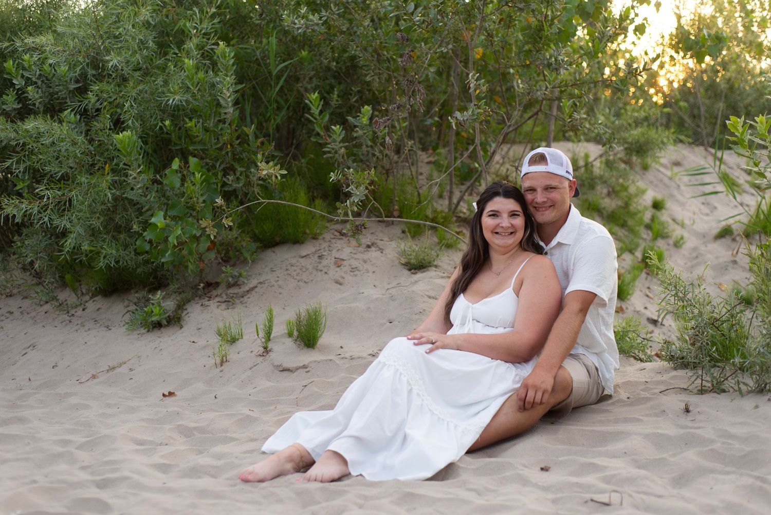 Two people in white outfits relaxing romantically on a sandy beach at sunset.