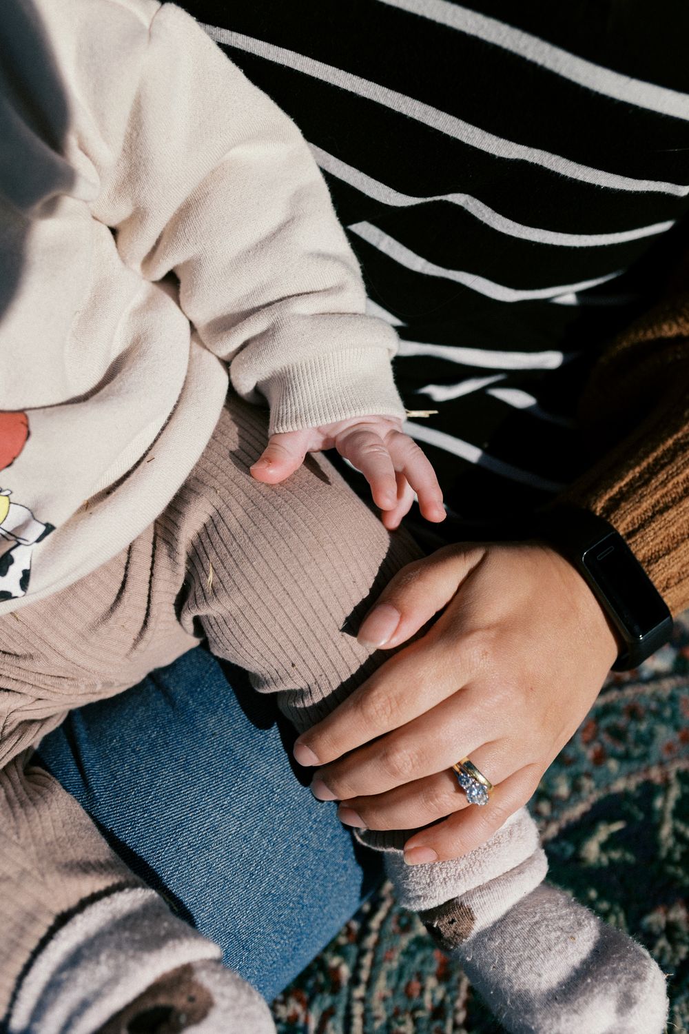 Person wearing cream colored sweater and blue jeans showing off an engagement ring on their hand.