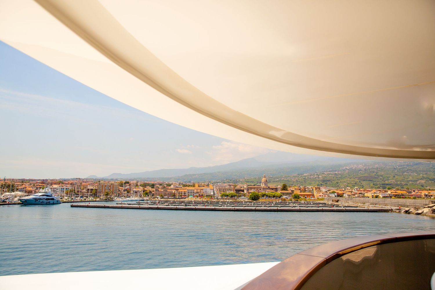 Coastal Mediterranean harbor view with boats and buildings under curved architectural detail.