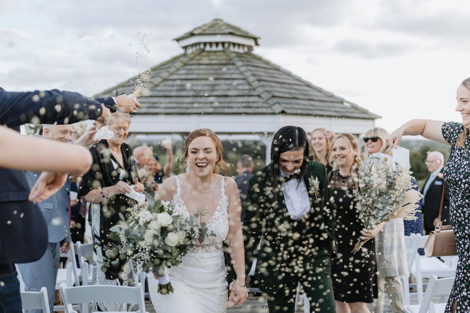 Wedding guests celebrate with confetti during an outdoor gazebo ceremony on a bright sunny day.
