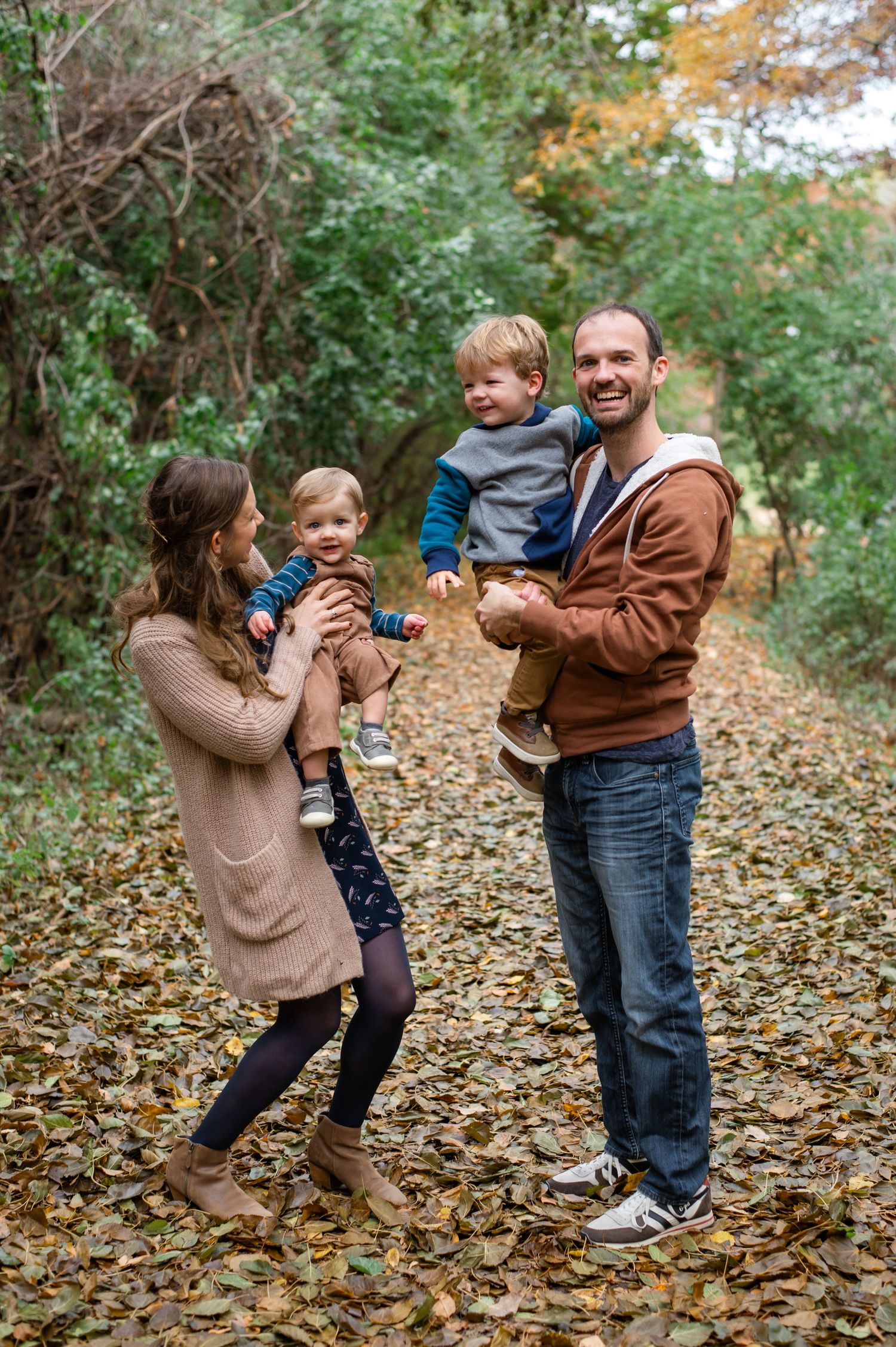 Family playing and having fun together in autumn leaves on a fall day in a wooded area.