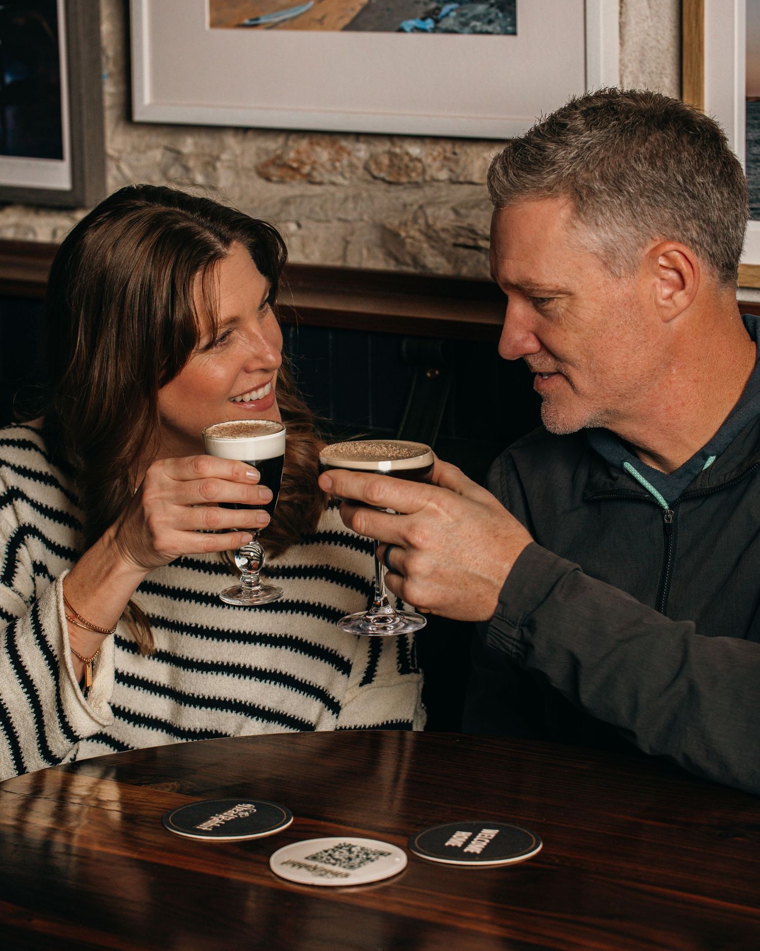 Couple in a restaurant sharing drinks and laughing together over a dark wooden table.