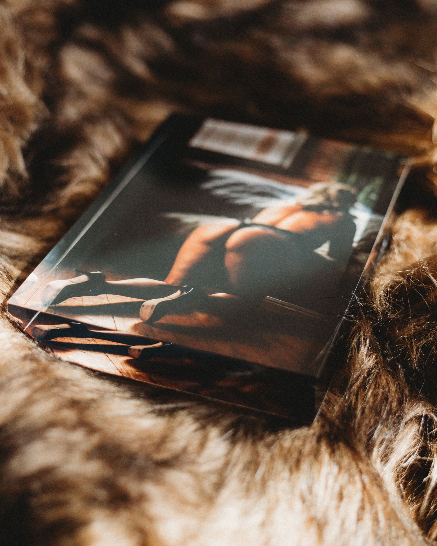 Multiple printed photographs scattered on a soft furry surface in warm, moody lighting.