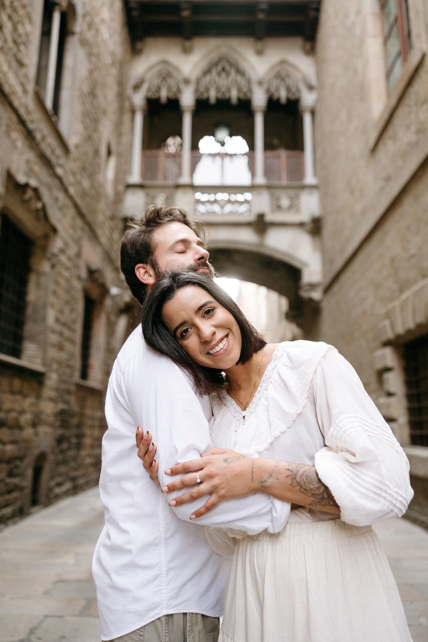 A playful couple in white clothing embraces in a historic stone alleyway.