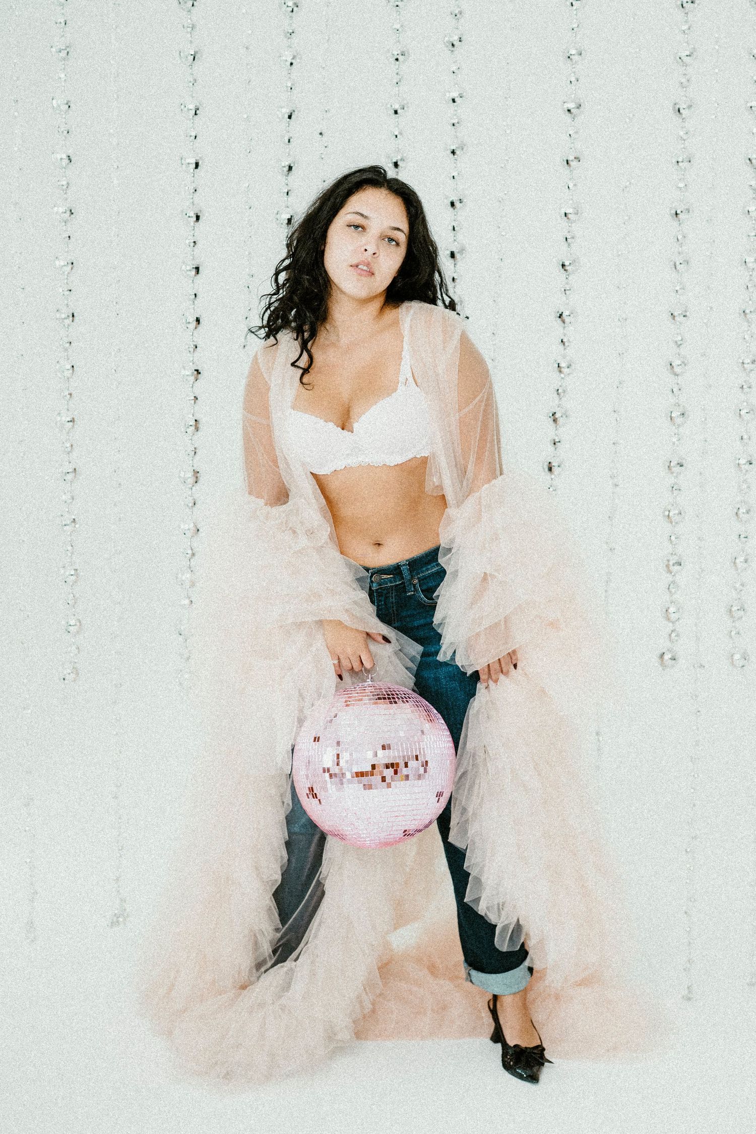A figure poses in a romantic pink tulle robe against a white backdrop for a dreamy boudoir photoshoot series.