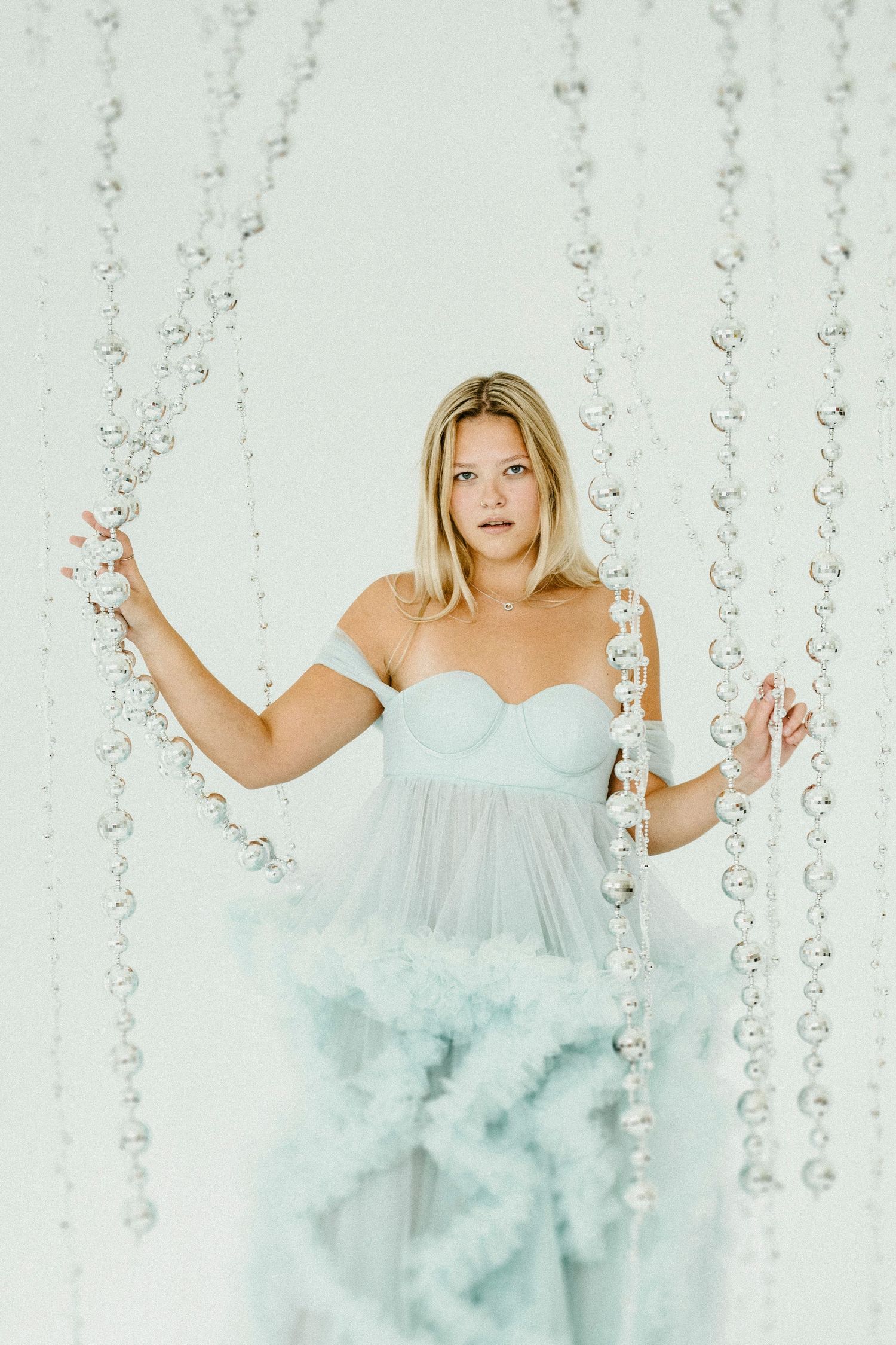 A dreamy portrait in a light blue tulle gown against crystal bead curtains creates an ethereal atmosphere.