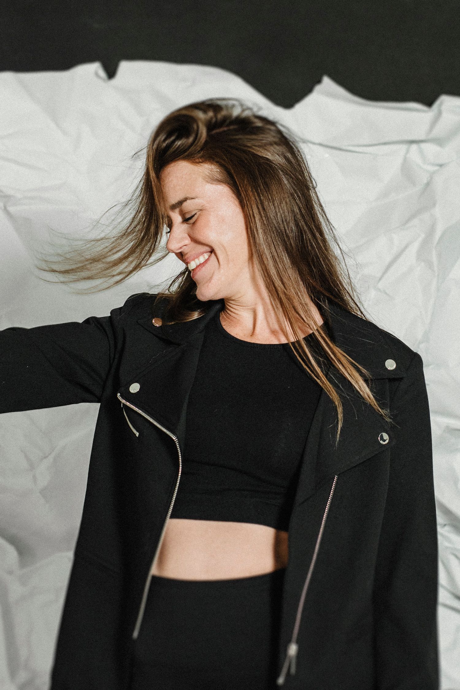 A model in a black leather jacket and crop top poses against a white backdrop in an artistic fashion photoshoot.