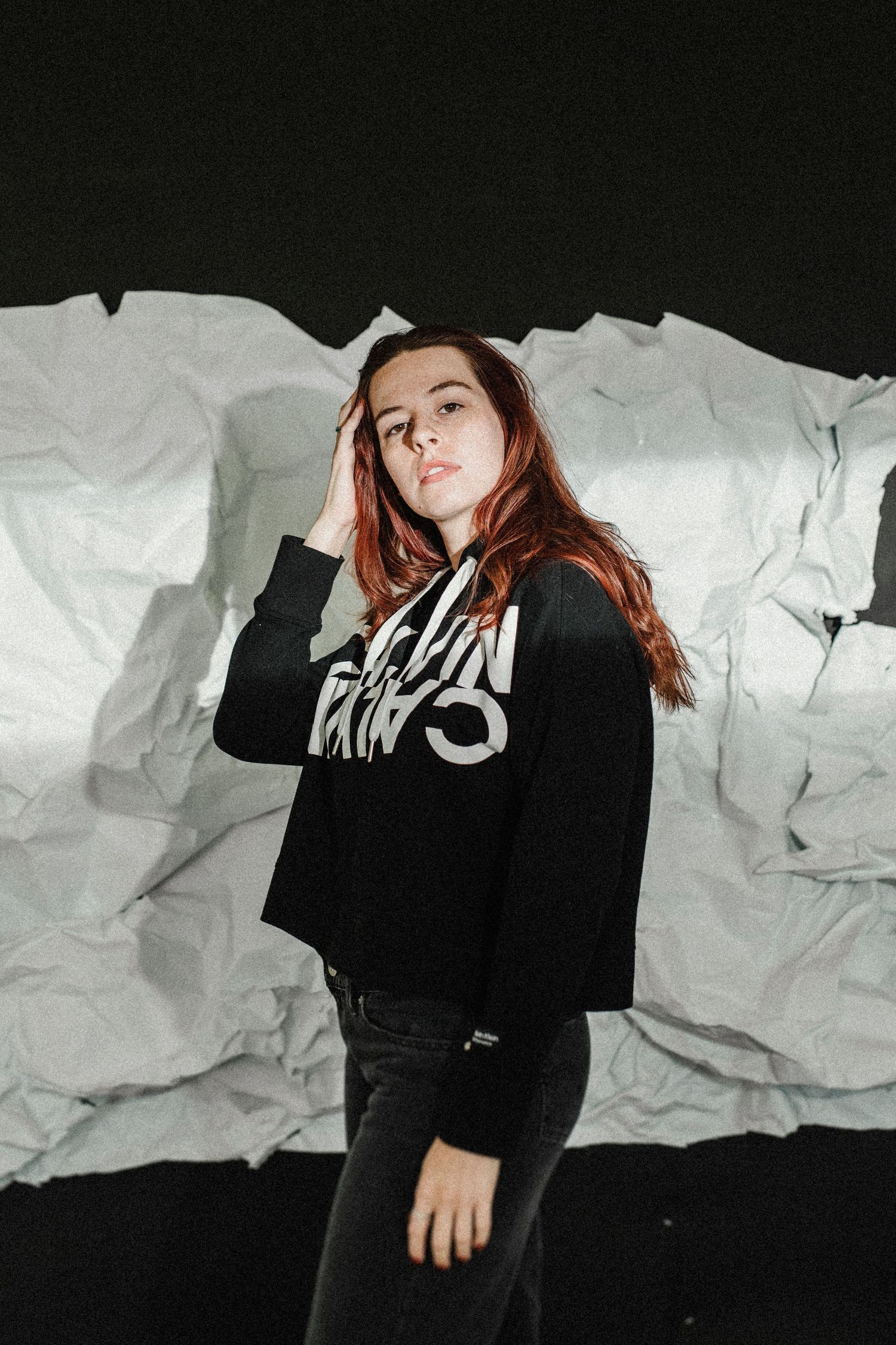 Artistic portrait showing figure in black against white crumpled paper backdrop creating dramatic shadows and contrast.