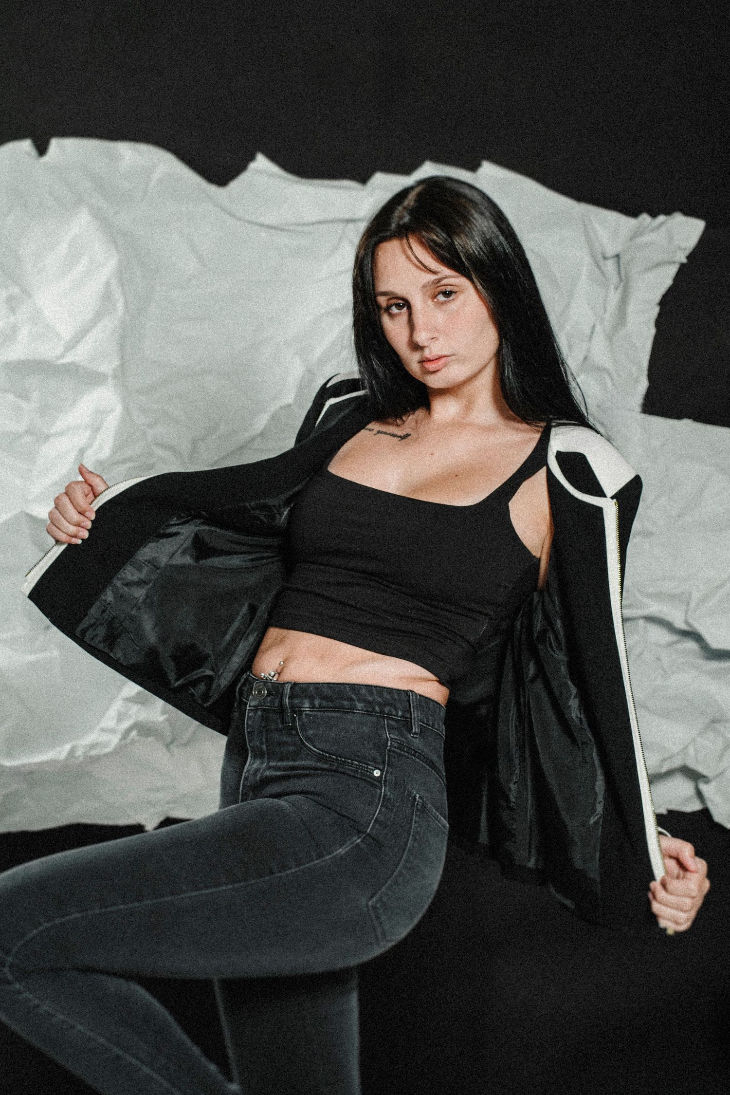 Woman posing in black top and dark jeans against white backdrop in stylish fashion photoshoot series.