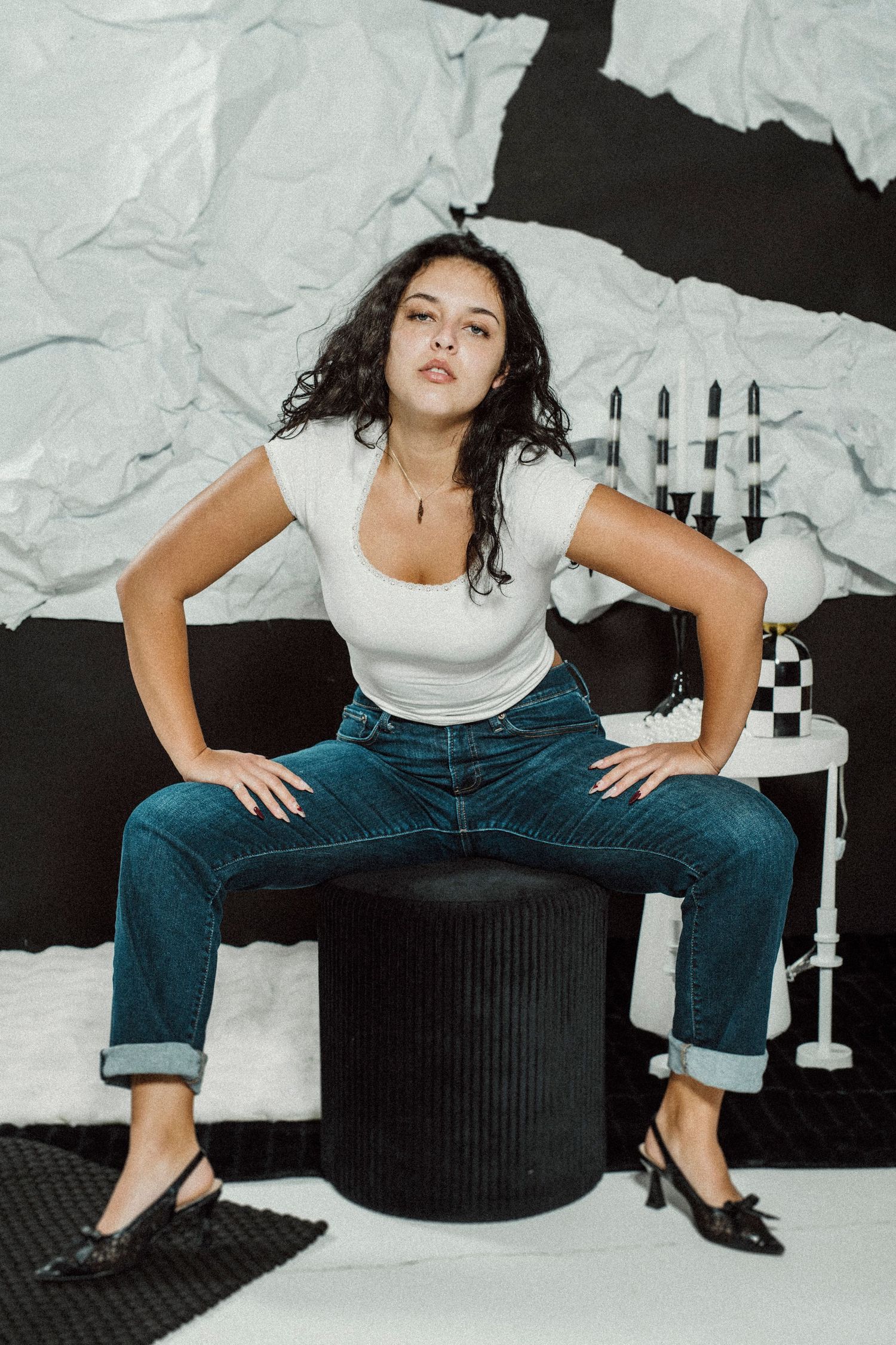 Artistic fashion photoshoot featuring a white top and dark jeans against a black and white textured backdrop.