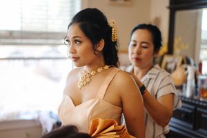 Elegant bridal preparation scene with gold jewelry and pink dress while getting ready in a sunlit room.