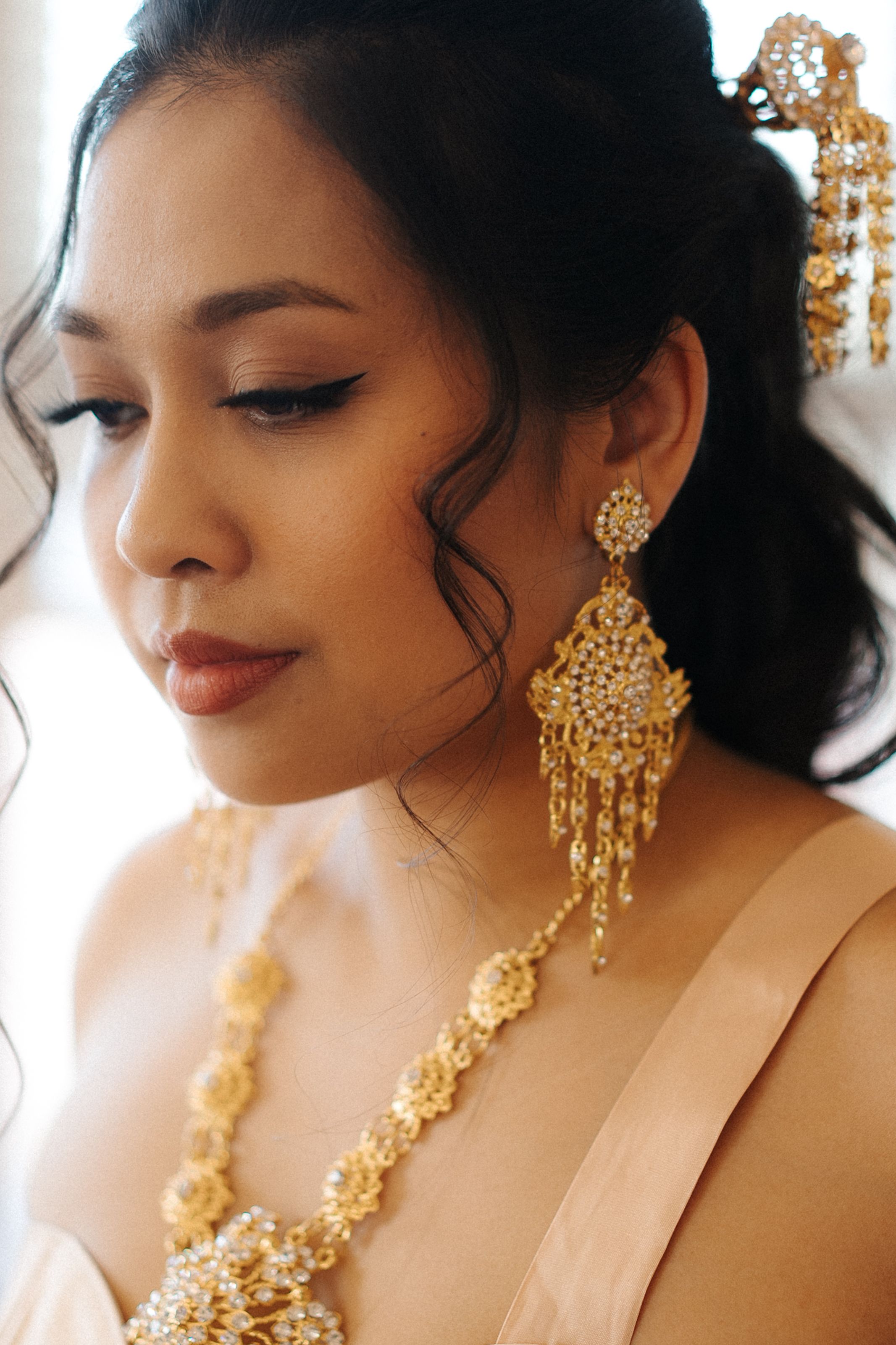 Elegant portrait featuring ornate gold chandelier earrings and matching necklace with delicate makeup and upswept hairstyle.