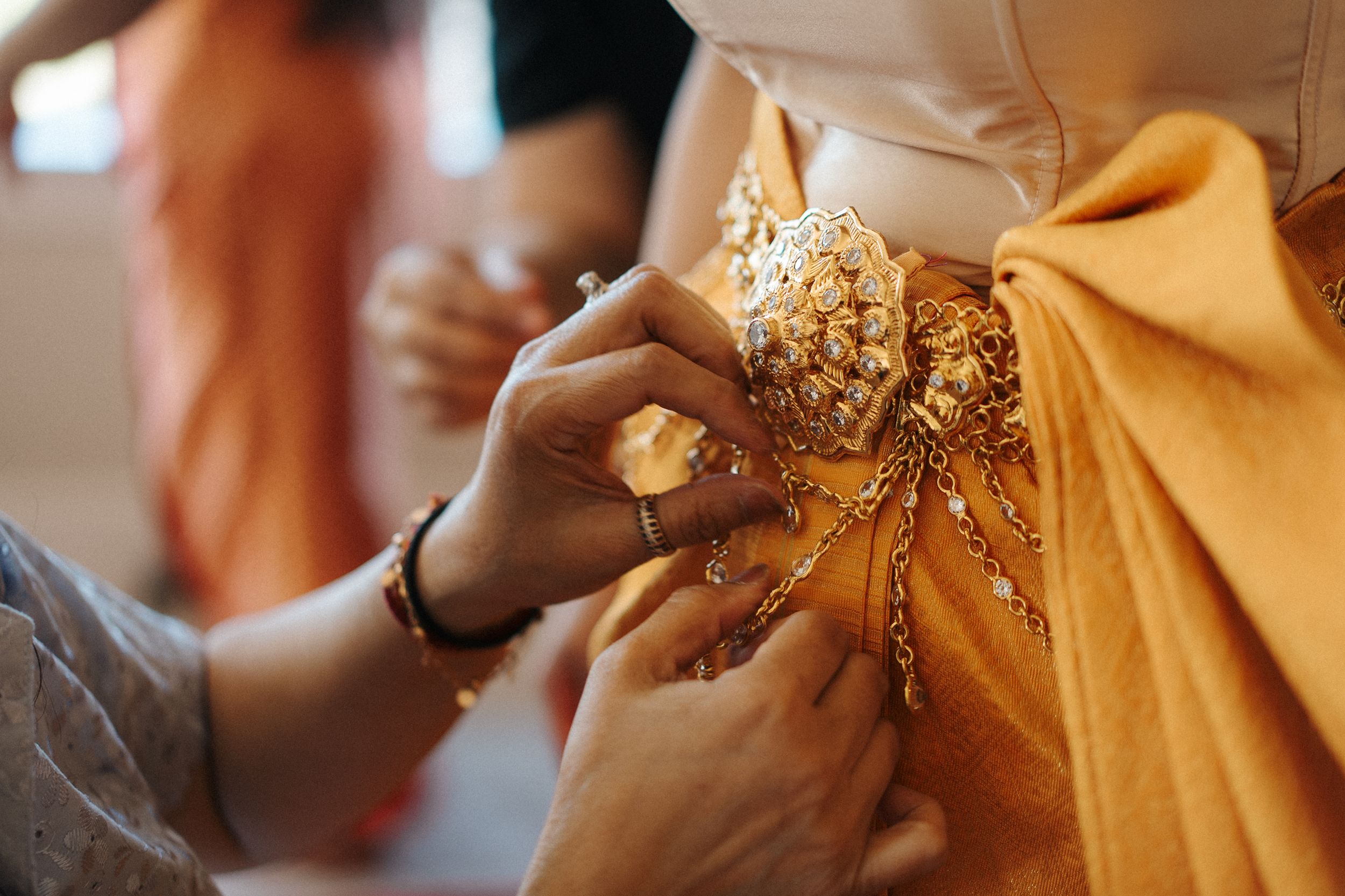 Close-up of hands adjusting intricate beaded embellishments on a golden yellow fabric during dress alterations.