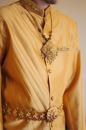 Ornate golden Thai traditional groom's outfit with intricate embellishments and decorative pendant necklace.