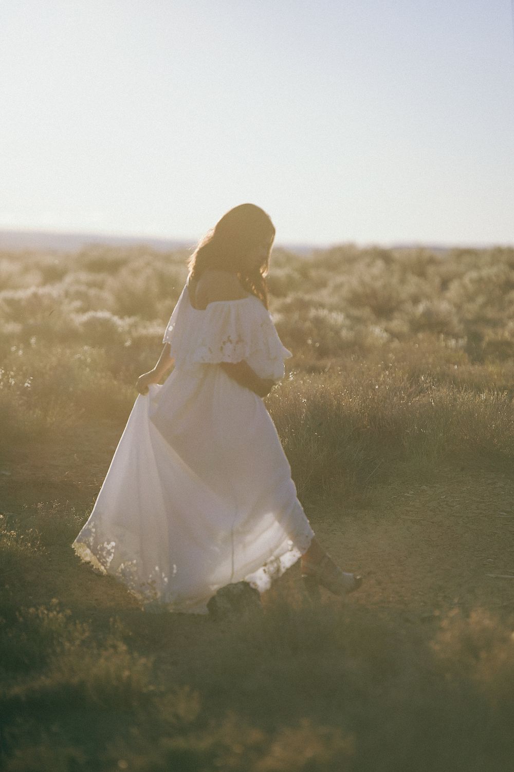 Ethereal backlit silhouette in flowing white dress against sunset sky.
