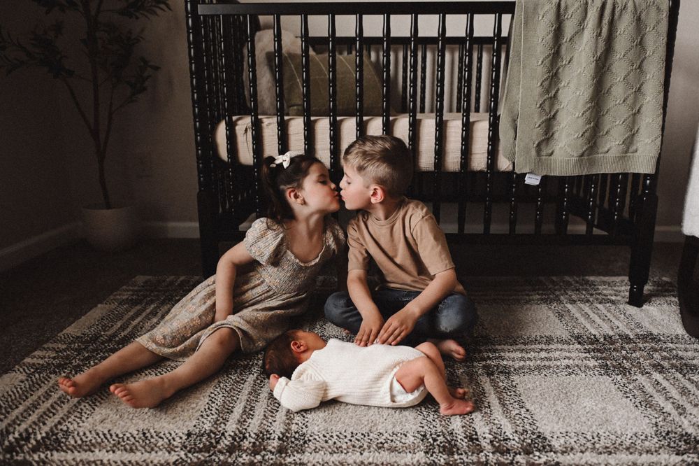 Mother and child lying together on a patterned rug in moody lighting.