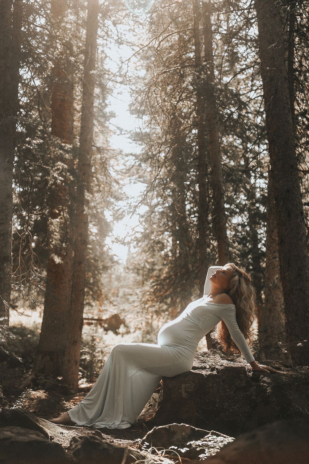 Dreamy forest maternity photos with sunlight streaming through tall trees.