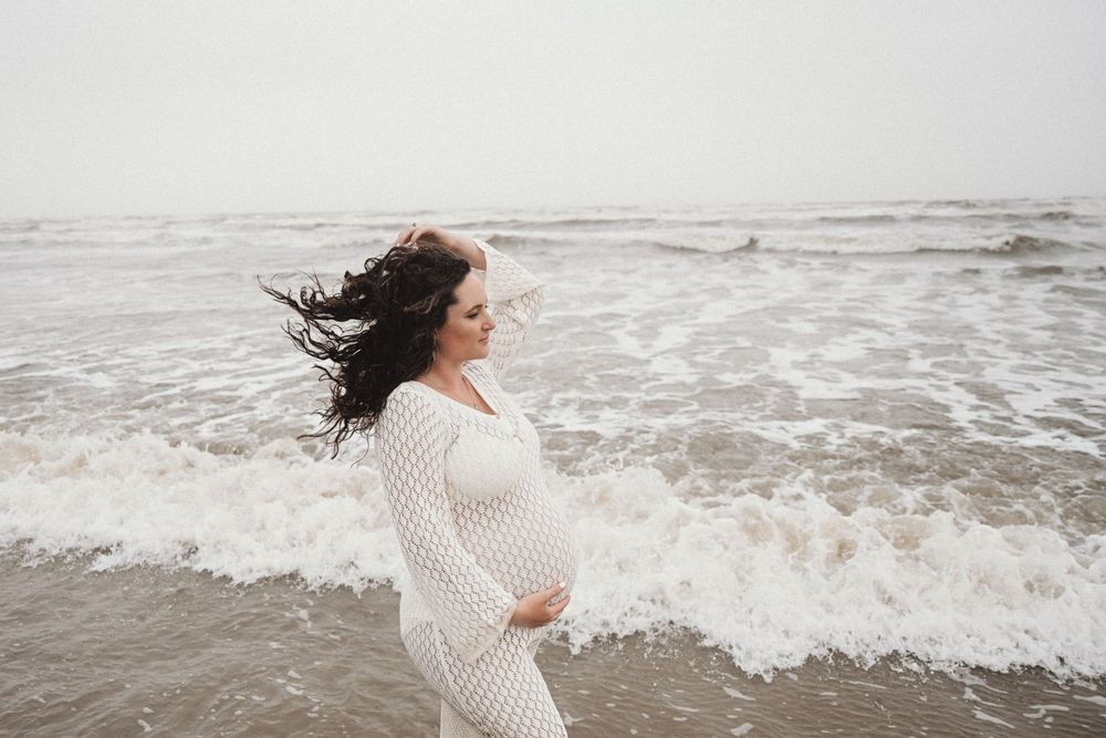 Romantic beach maternity session with white knit sweater and crashing waves.